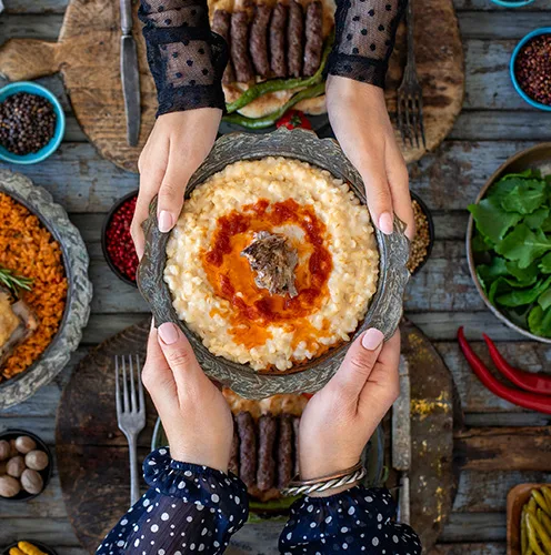 Vibrant bowl of creamy porridge topped with meat and spicy sauce, accompanied by colorful sides.