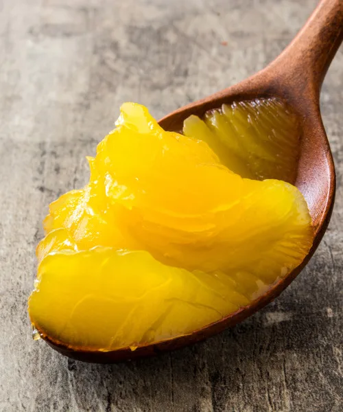 Golden canned mango pulp and fruit segments on a wooden spoon, showcasing premium quality citrus product for food service and wholesale distribution.
